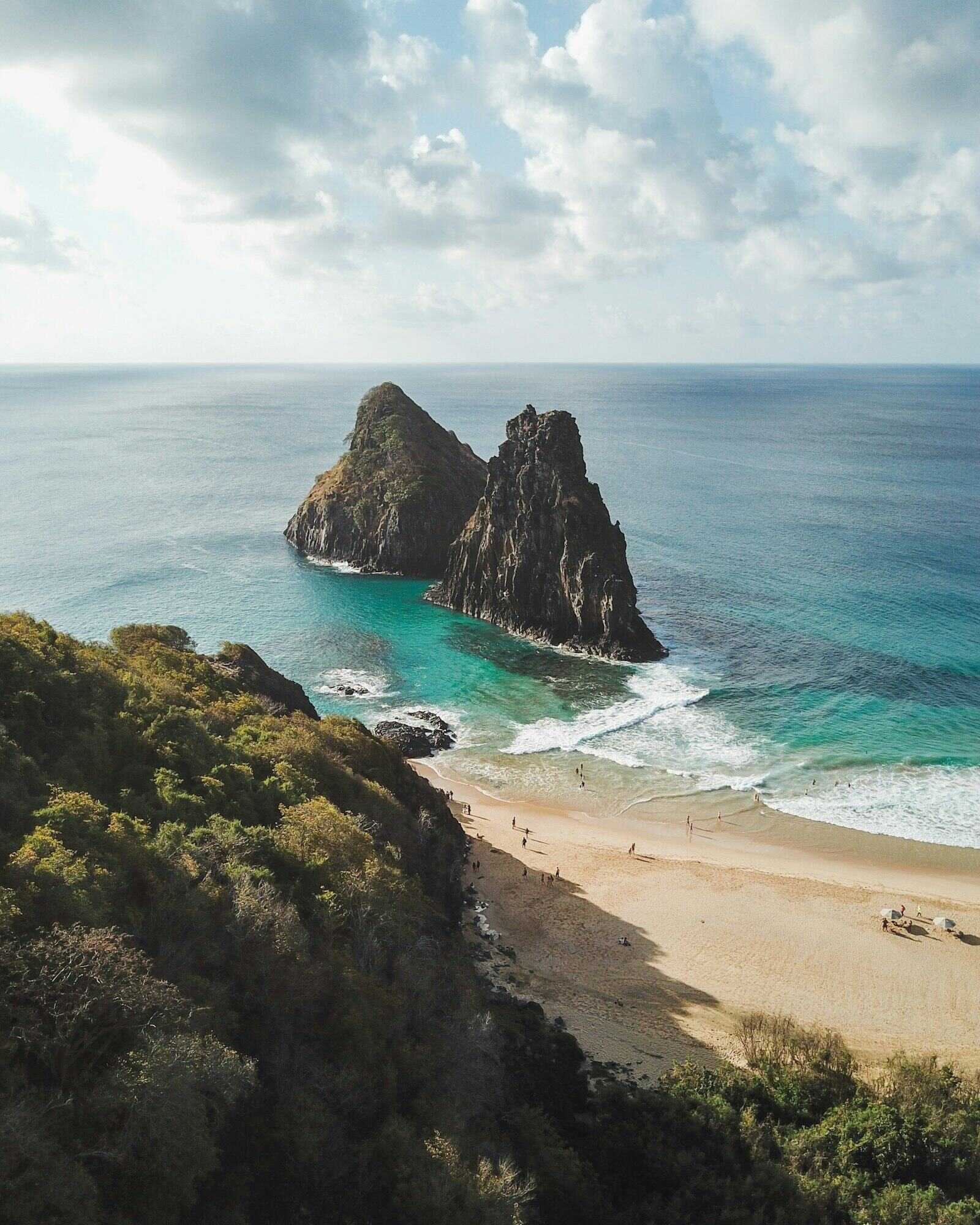 Formação rochosa cercada de vegetação diante do mar
